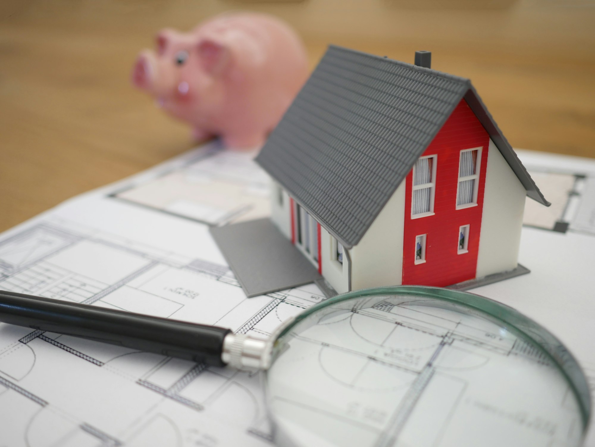 Maqueta de casa sobre planos con lupa, símbolo de valoración inmobiliaria